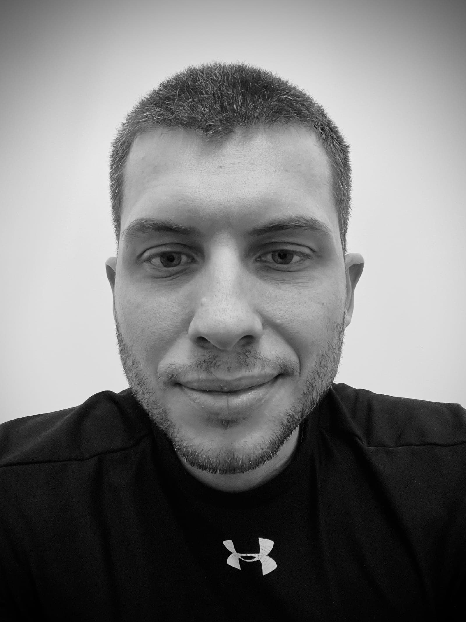 Close-up black-and-white portrait of Nazar Khomyshyn looking at the camera with a slight smile, in a black t-shirt against a plain light background.